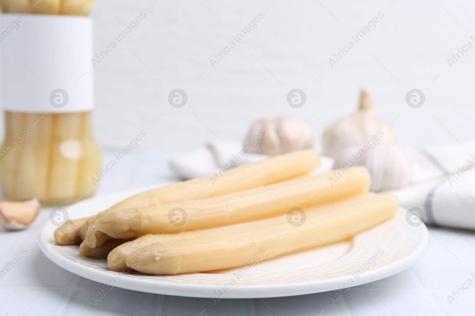 Photo of Pickled asparagus and garlic on white tiled table, closeup