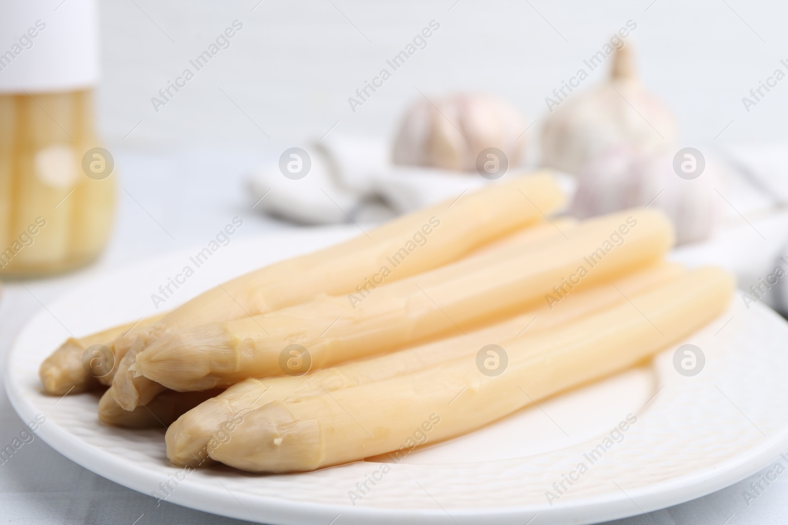 Photo of Pickled asparagus and garlic on white tiled table, closeup
