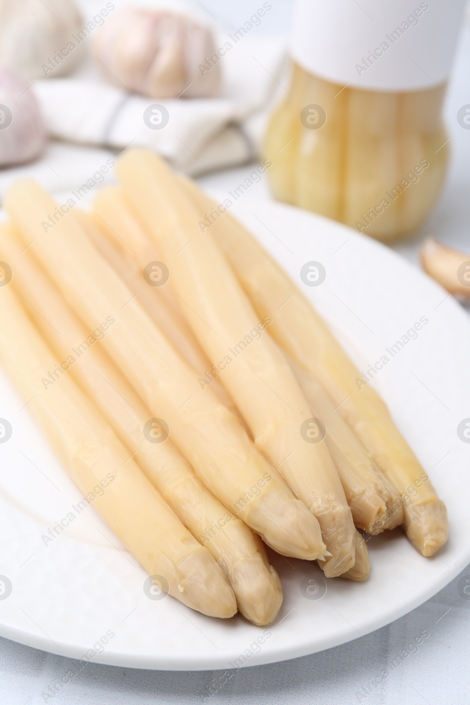 Photo of Pickled asparagus and garlic on white tiled table, closeup