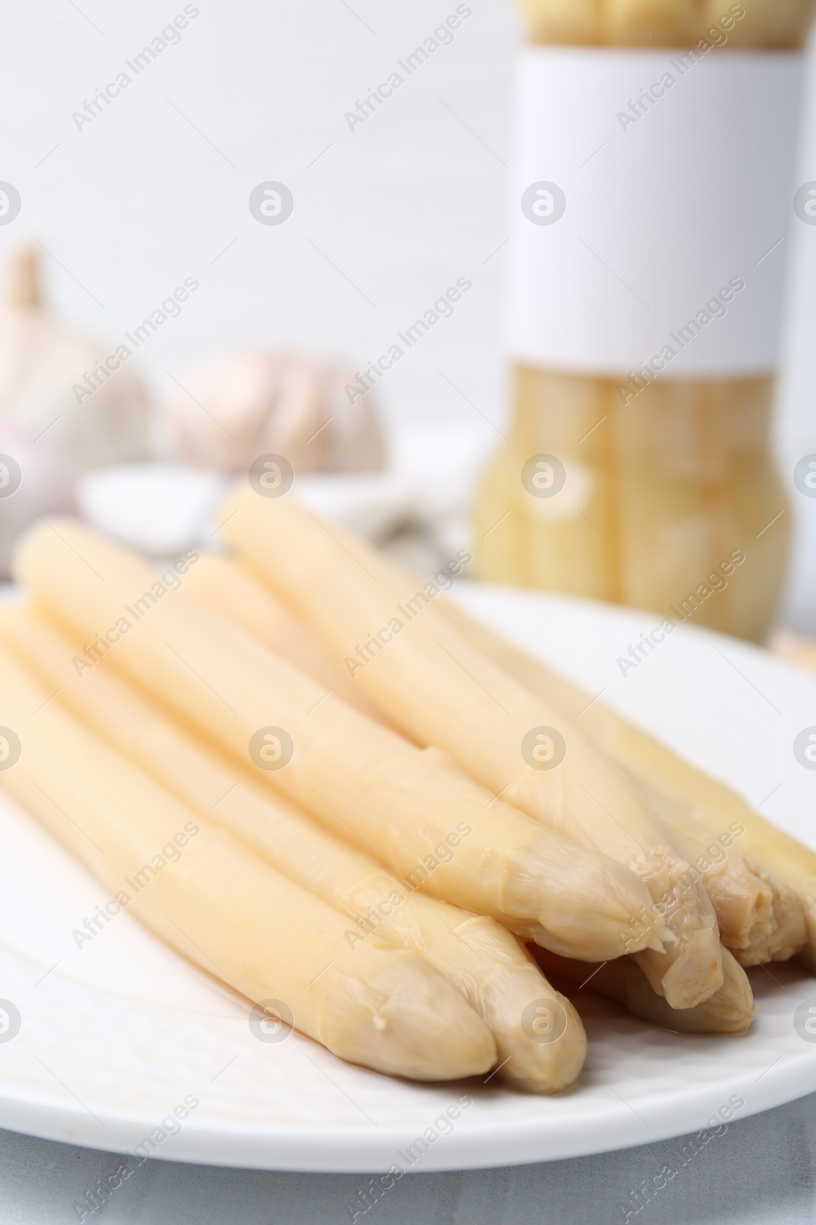 Photo of Pickled asparagus and garlic on white tiled table, closeup