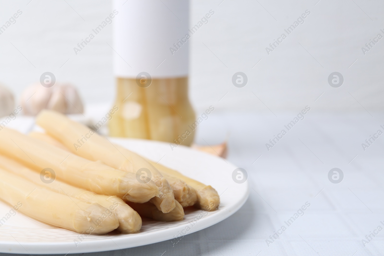 Photo of Pickled asparagus and garlic on white tiled table, closeup. Space for text