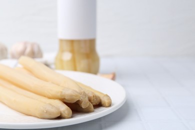 Photo of Pickled asparagus and garlic on white tiled table, closeup. Space for text