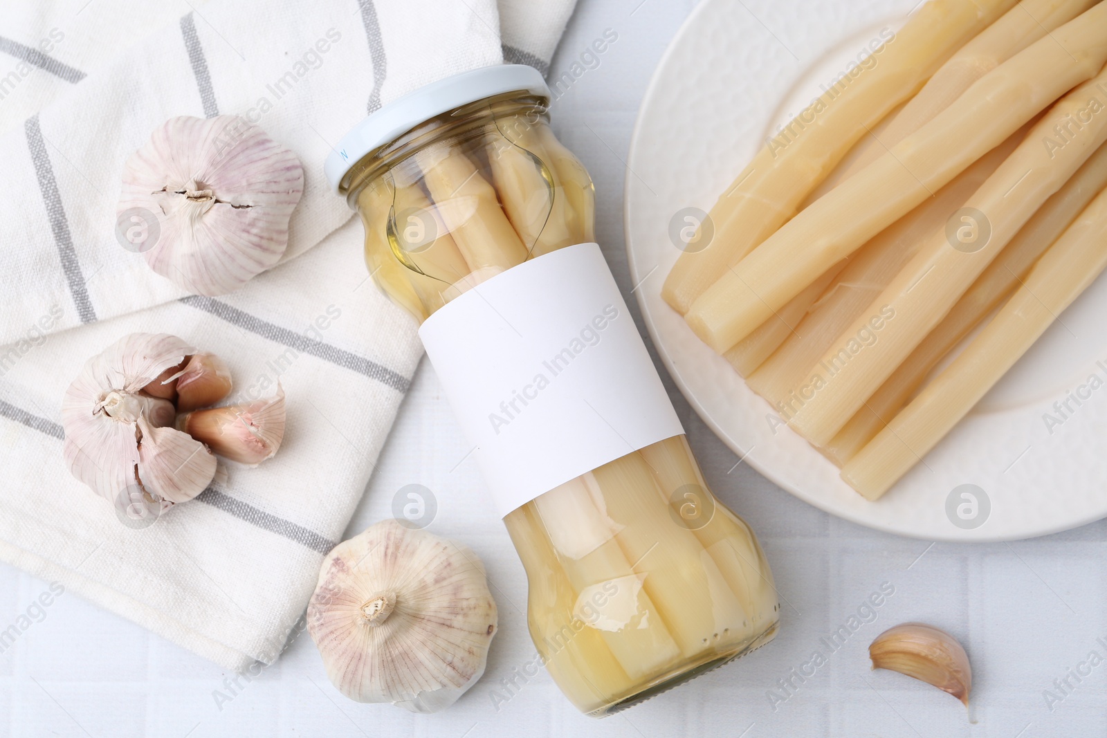 Photo of Pickled asparagus and garlic on white tiled table, flat lay