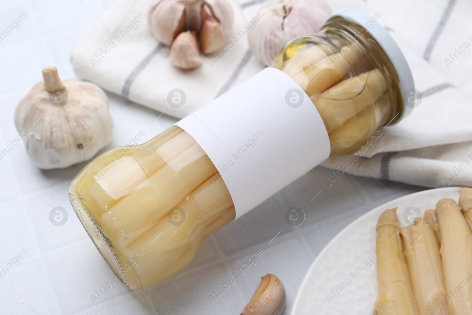 Photo of Pickled asparagus and garlic on white tiled table, closeup
