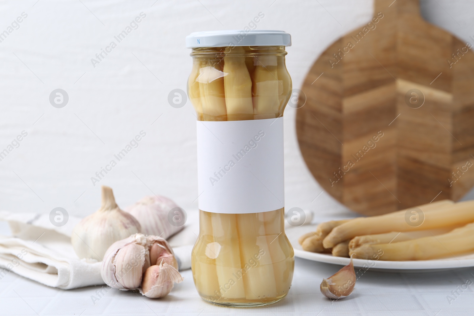 Photo of Pickled asparagus and garlic on white tiled table