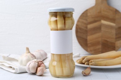 Photo of Pickled asparagus and garlic on white tiled table
