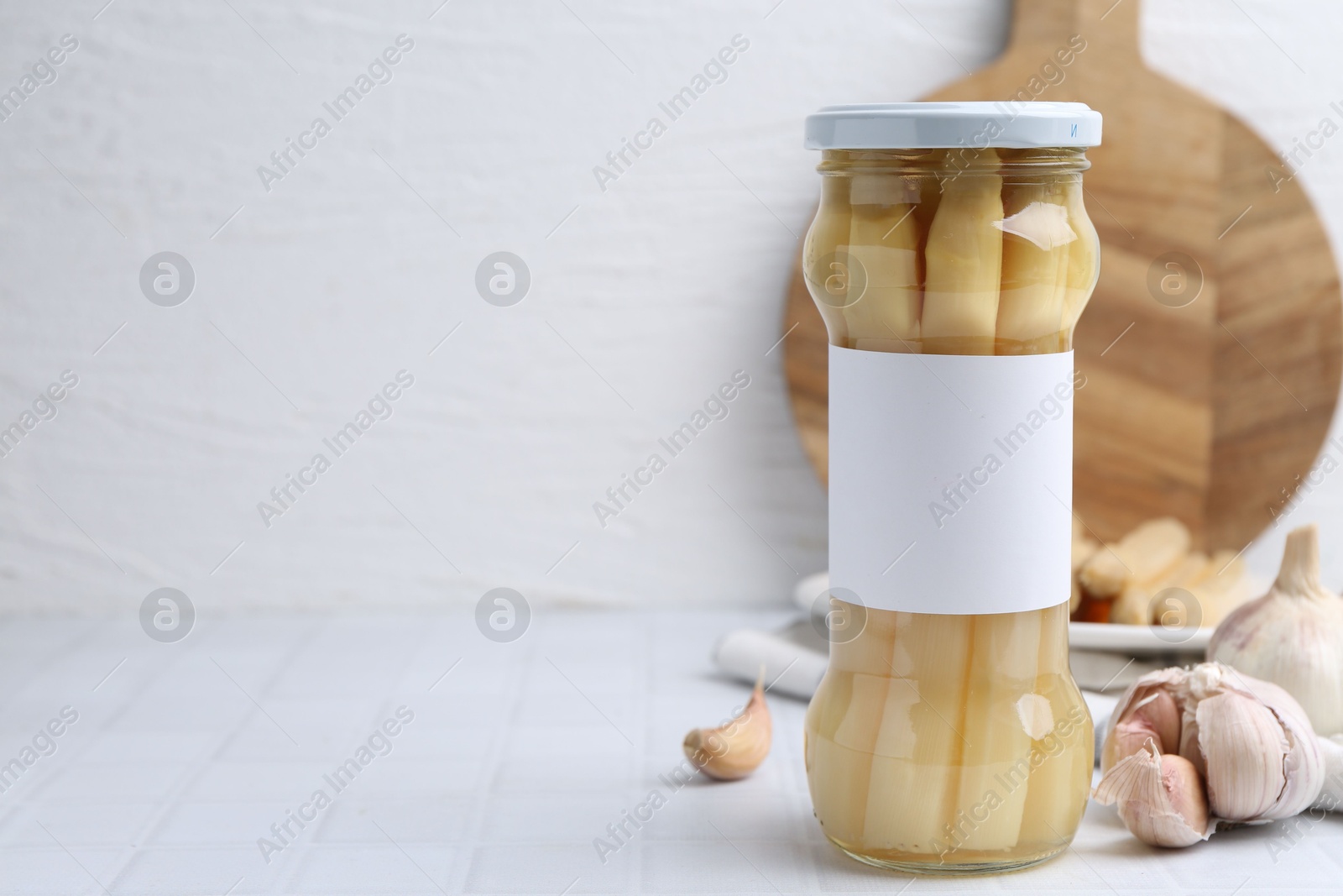 Photo of Pickled asparagus and garlic on white tiled table. Space for text