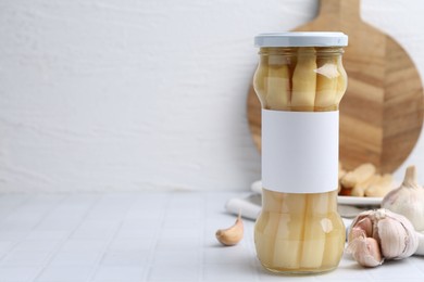 Photo of Pickled asparagus and garlic on white tiled table. Space for text