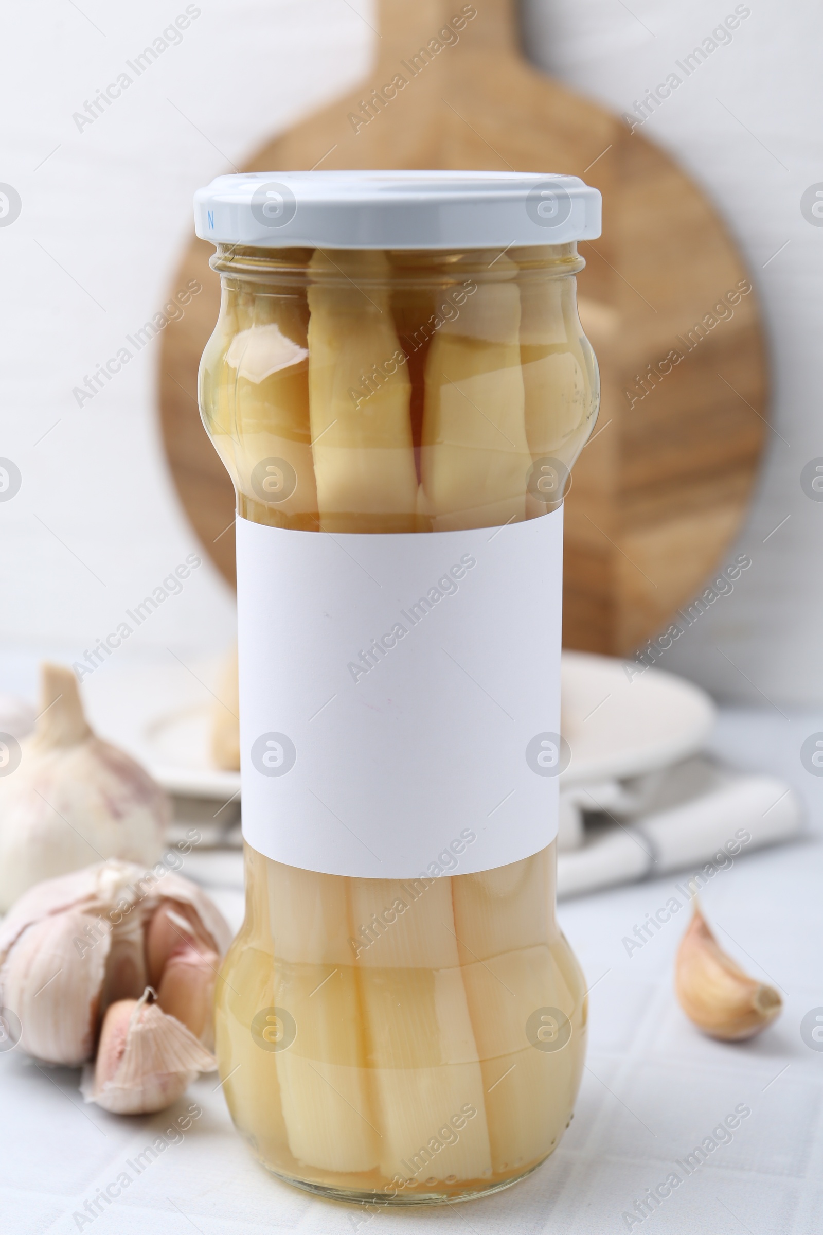 Photo of Pickled asparagus and garlic on white tiled table, closeup