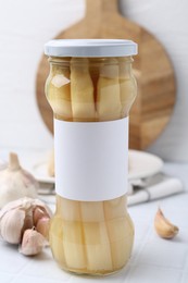Photo of Pickled asparagus and garlic on white tiled table, closeup
