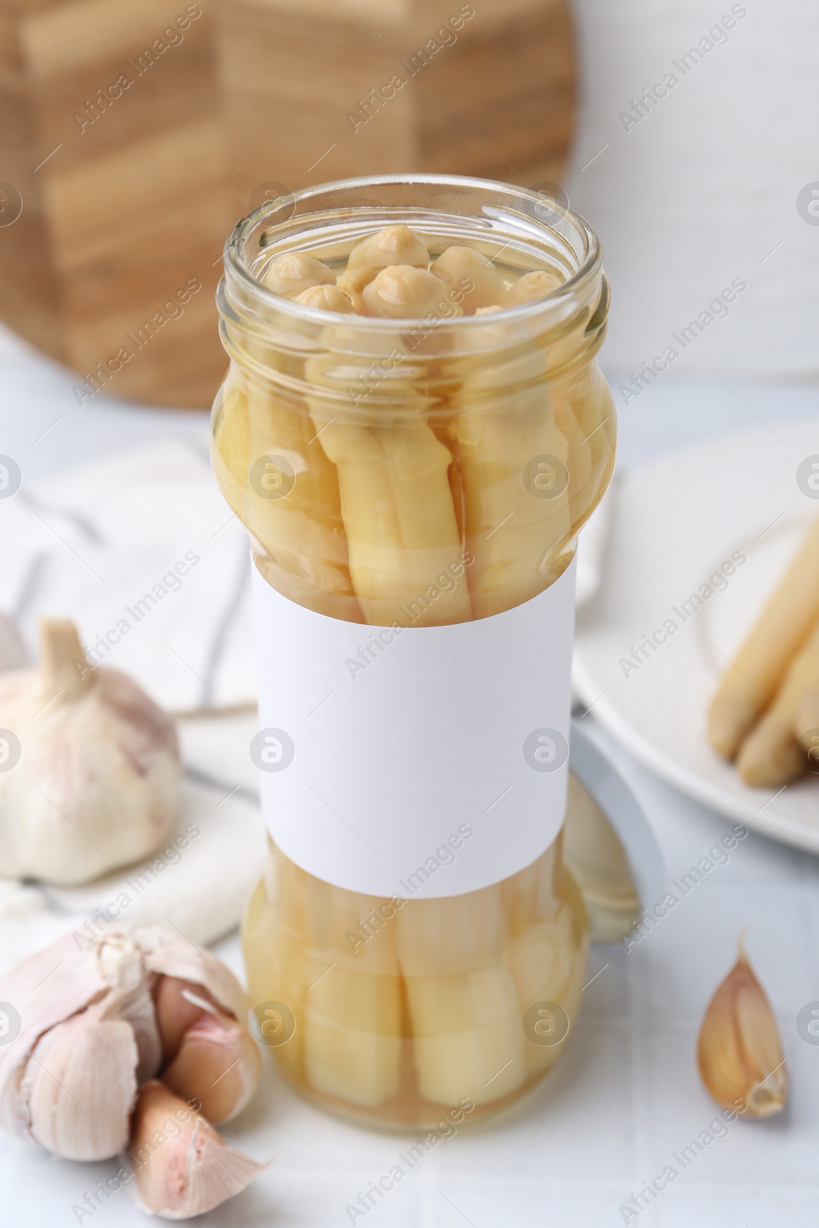 Photo of Pickled asparagus and garlic on white tiled table, closeup