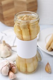 Photo of Pickled asparagus and garlic on white tiled table, closeup