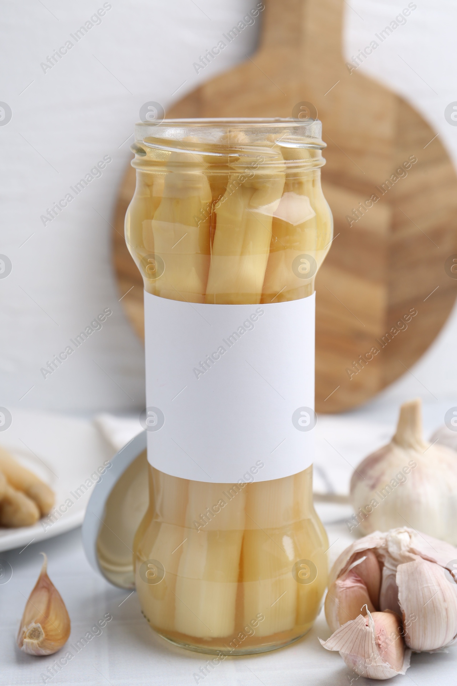 Photo of Pickled asparagus and garlic on white tiled table, closeup