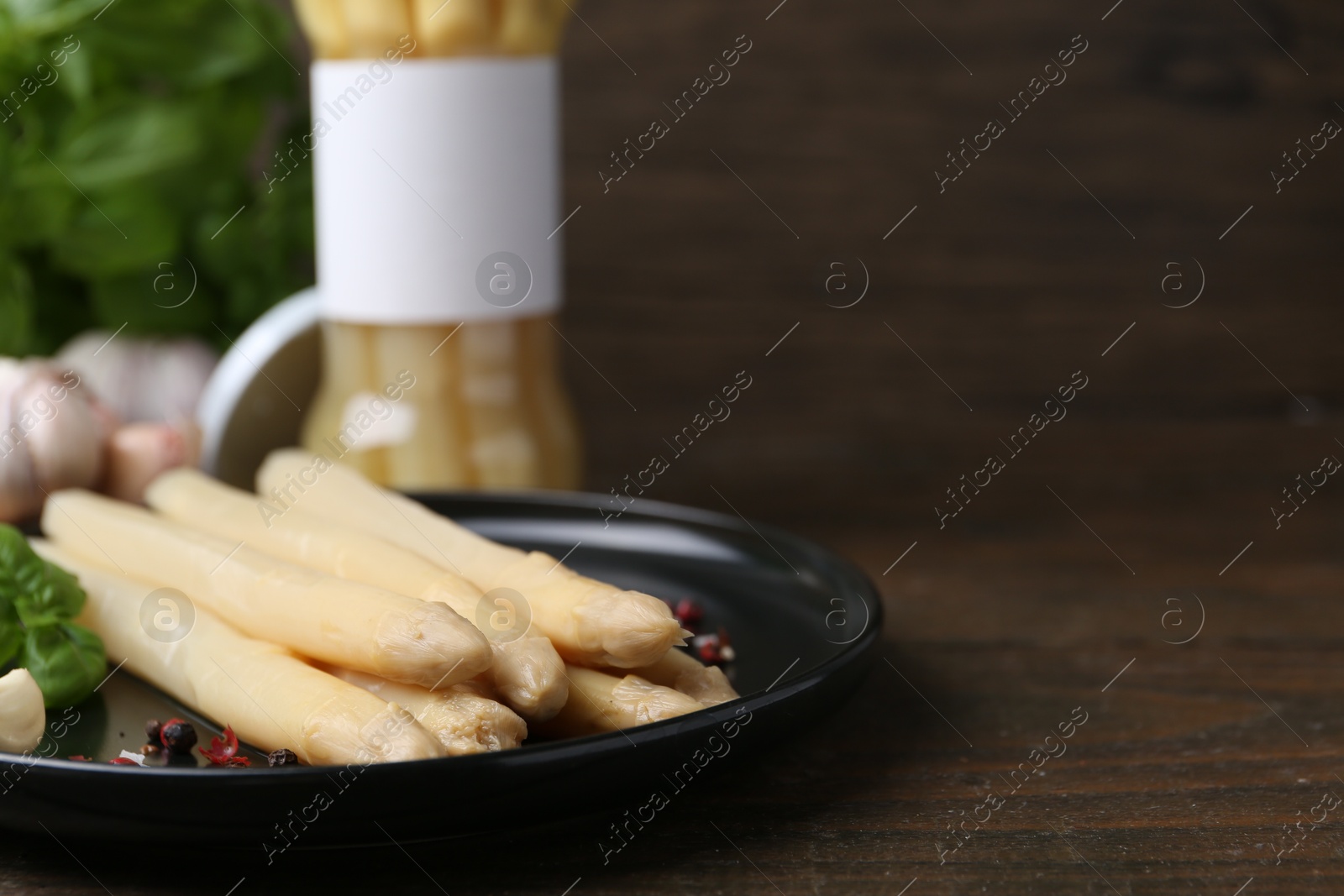 Photo of Pickled asparagus and spices on wooden table, closeup. Space for text