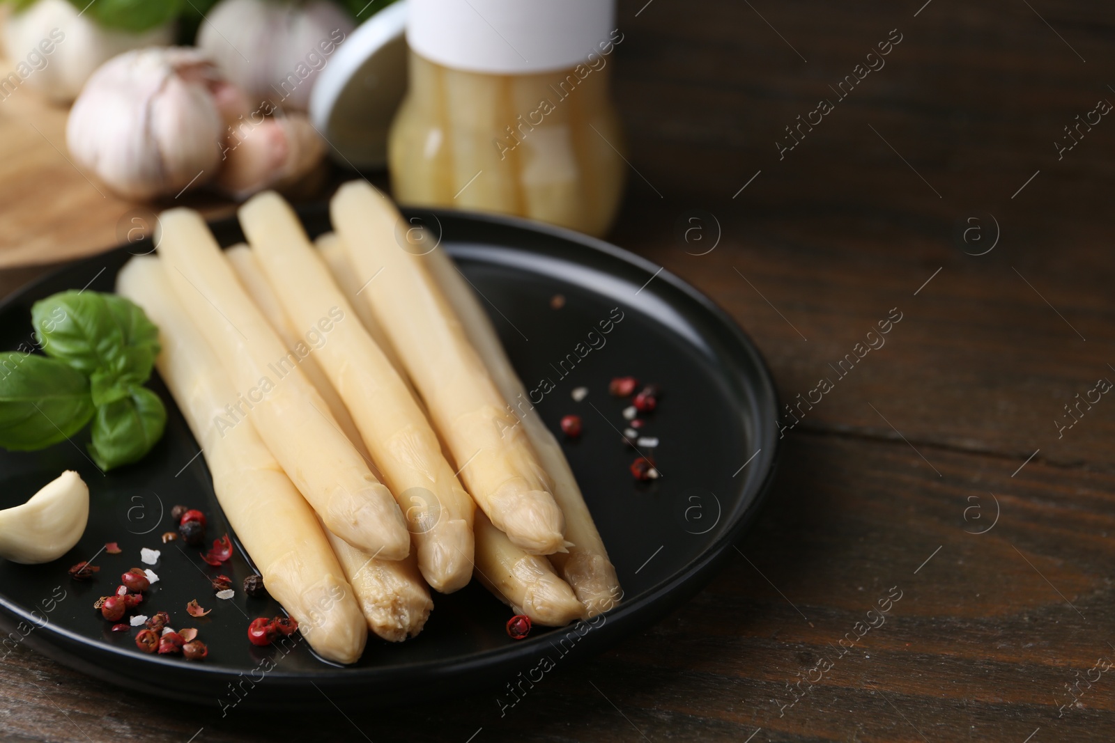 Photo of Pickled asparagus and spices on wooden table, closeup. Space for text