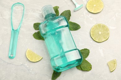 Photo of Mouthwash, other oral hygiene products, mint and lime slices on light marble table, closeup