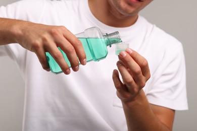 Photo of Man pouring mouthwash into cap on light grey background, closeup