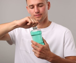 Photo of Man with bottle of mouthwash on light grey background, closeup