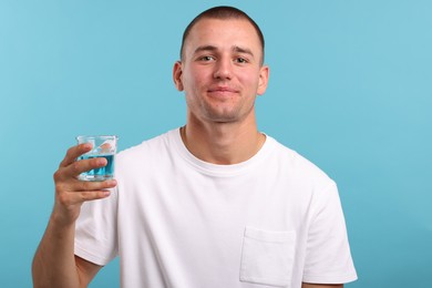Photo of Man with glass of mouthwash on light blue background