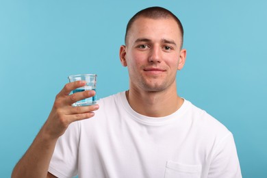 Photo of Man with glass of mouthwash on light blue background