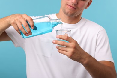 Photo of Man pouring mouthwash into glass on light blue background, closeup
