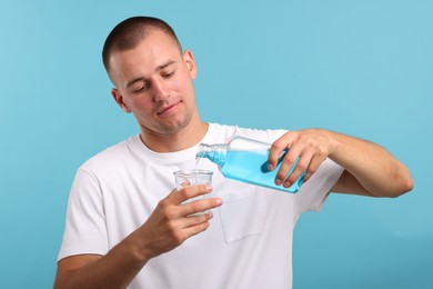 Photo of Man pouring mouthwash into glass on light blue background