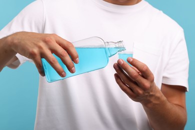 Photo of Man pouring mouthwash into cap on light blue background, closeup