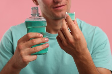Photo of Man with bottle and cap of mouthwash on pink background, closeup