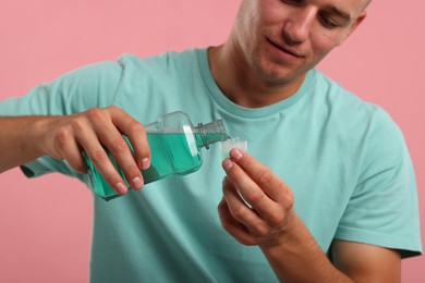 Photo of Man pouring mouthwash into cap on pink background, closeup