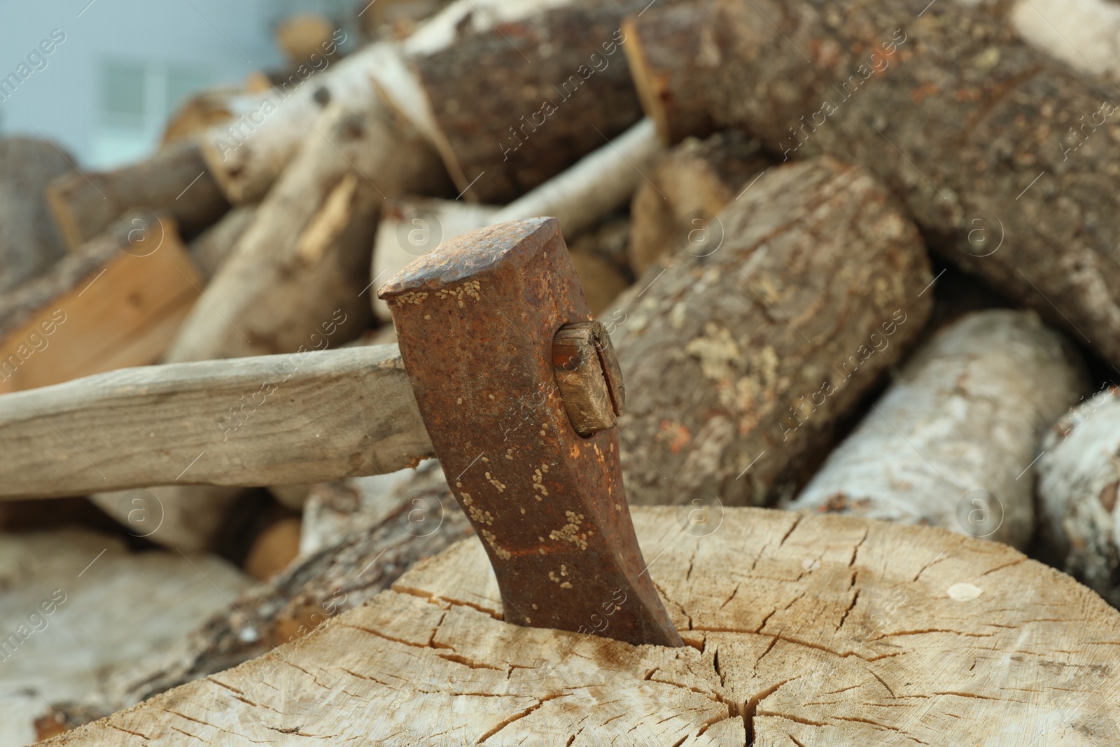 Photo of Axe in stump and pile of cut firewood outdoors, closeup