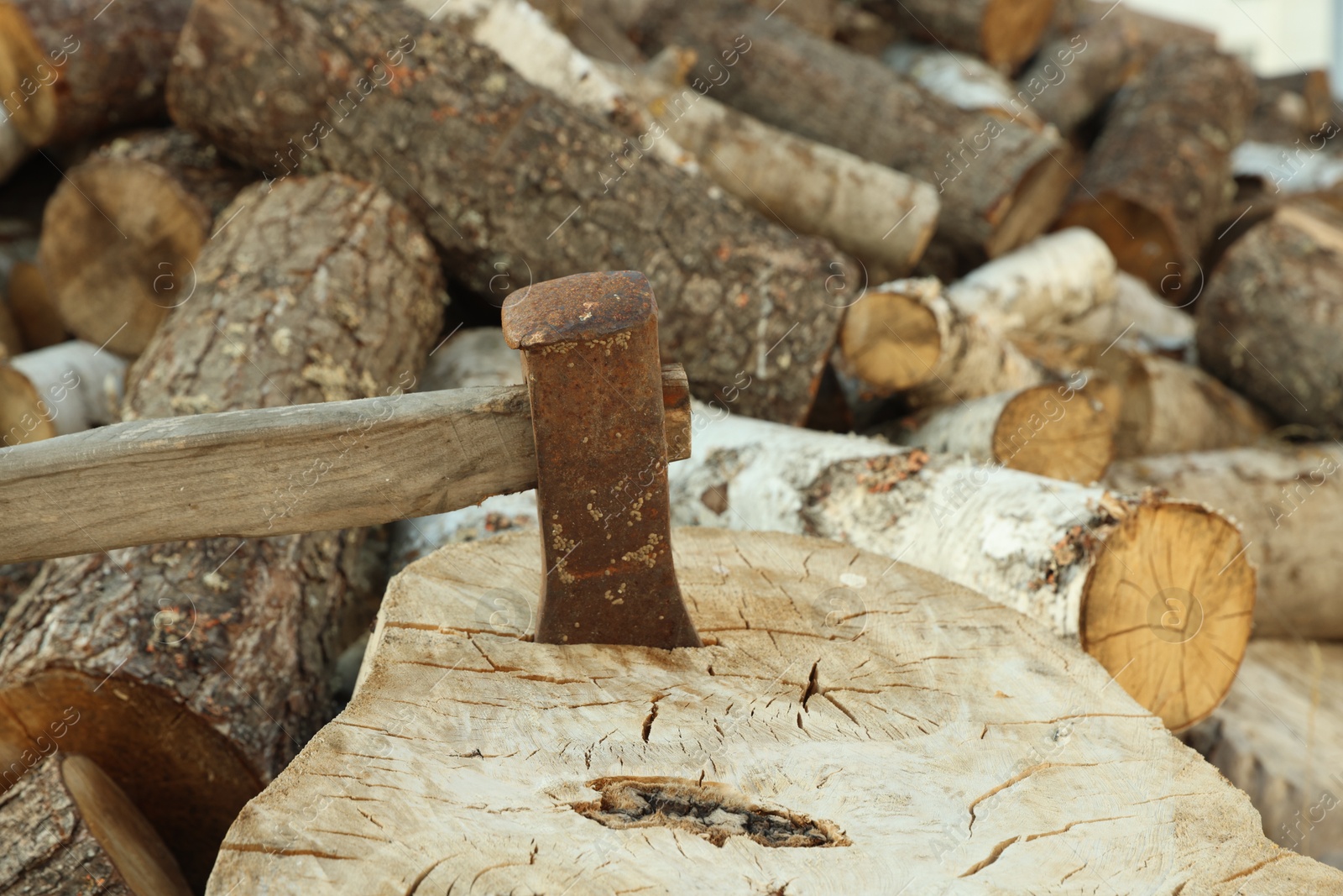 Photo of Axe in stump and pile of cut firewood outdoors, closeup
