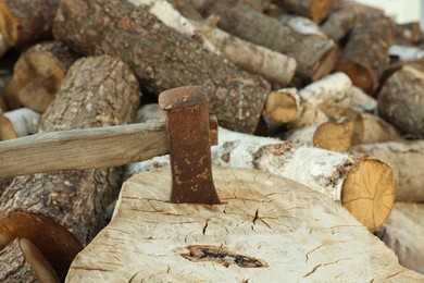 Photo of Axe in stump and pile of cut firewood outdoors, closeup