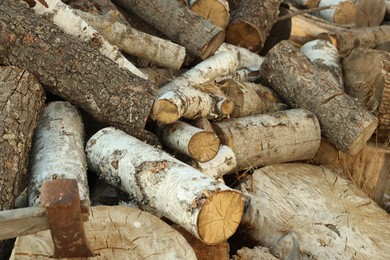 Photo of Axe in stump and pile of cut firewood outdoors, closeup