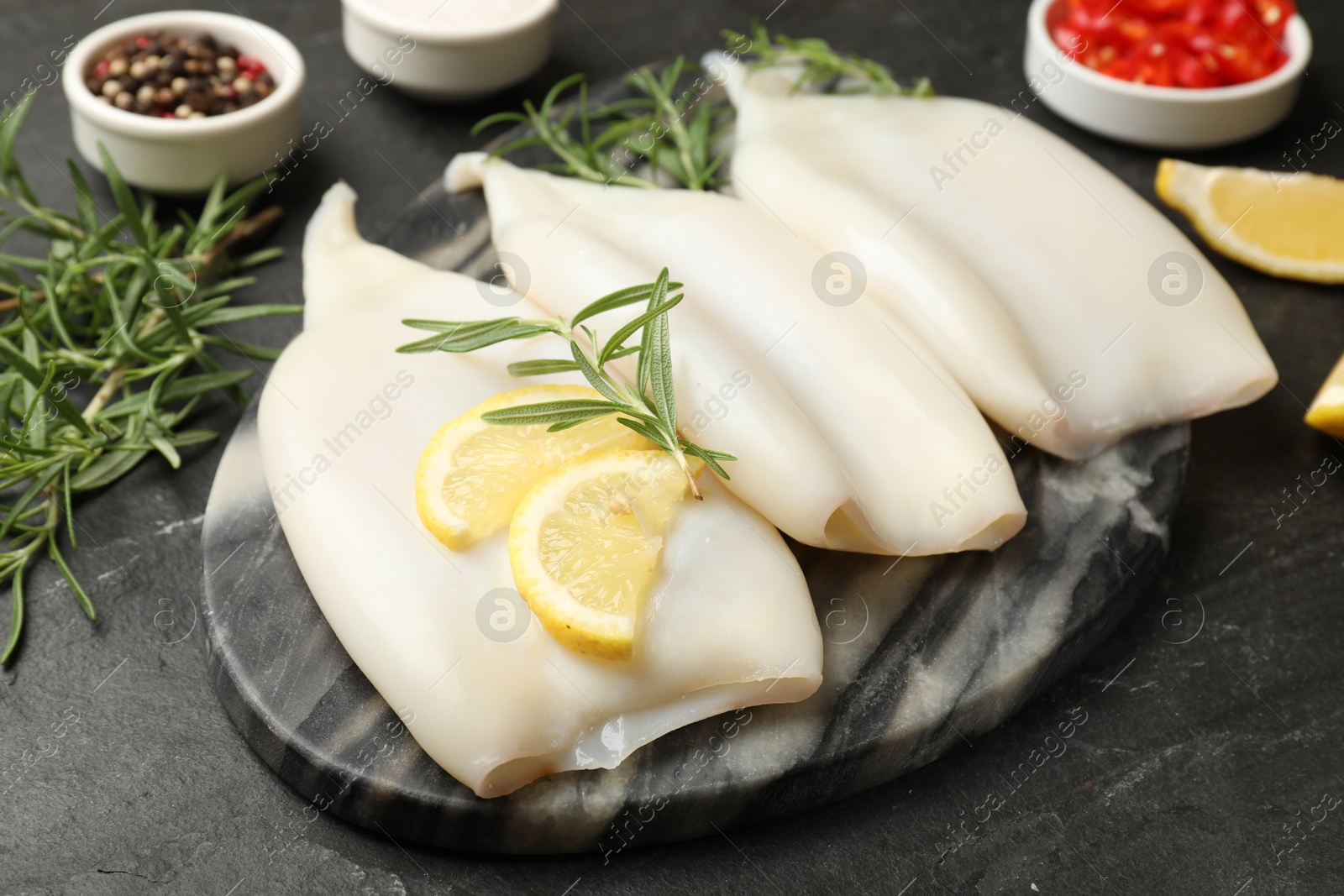 Uncooked squids with lemon slices, rosemary and spices on black table, closeup Photo of Uncooked squids with lemon slices, rosemary and spices on black table, closeup