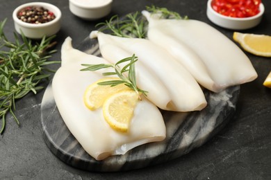 Photo of Uncooked squids with lemon slices, rosemary and spices on black table, closeup