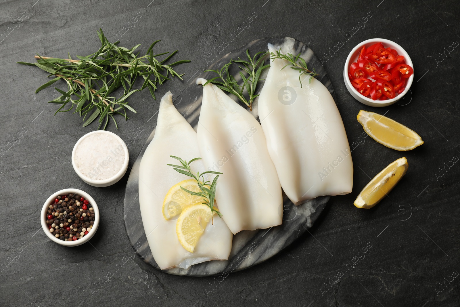 Uncooked squids with lemon slices, rosemary and spices on black table, flat lay Photo of Uncooked squids with lemon slices, rosemary and spices on black table, flat lay