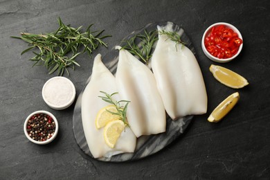 Photo of Uncooked squids with lemon slices, rosemary and spices on black table, flat lay