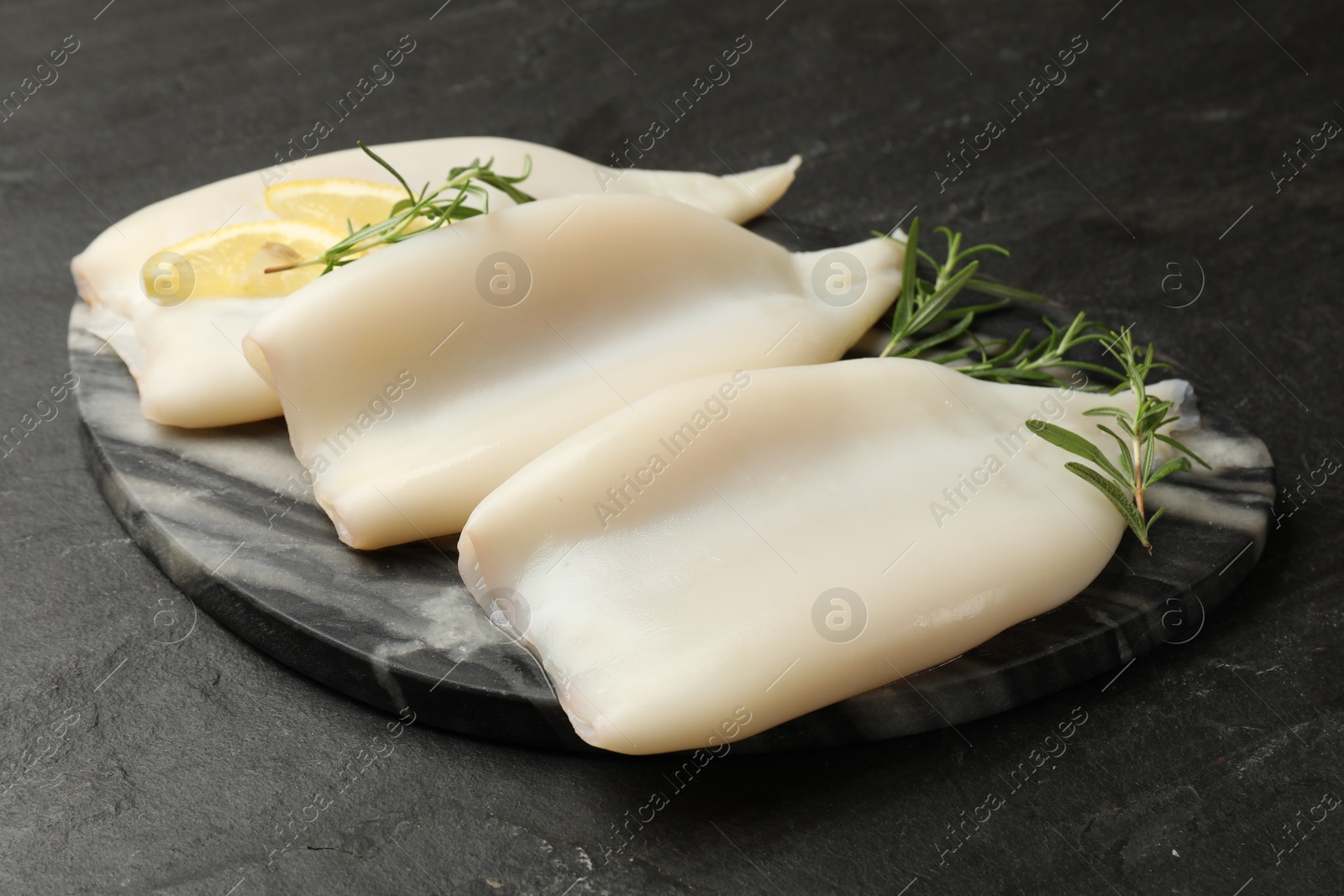 Uncooked squids with lemon slices and rosemary on black table, closeup Photo of Uncooked squids with lemon slices and rosemary on black table, closeup