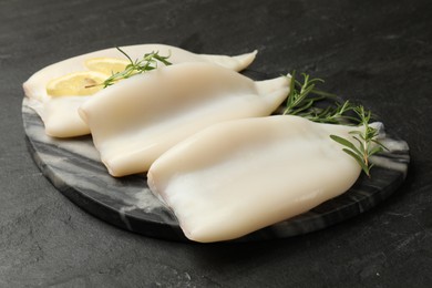 Photo of Uncooked squids with lemon slices and rosemary on black table, closeup