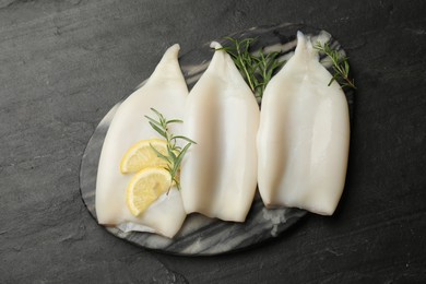 Photo of Uncooked squids with lemon slices and rosemary on black table, top view