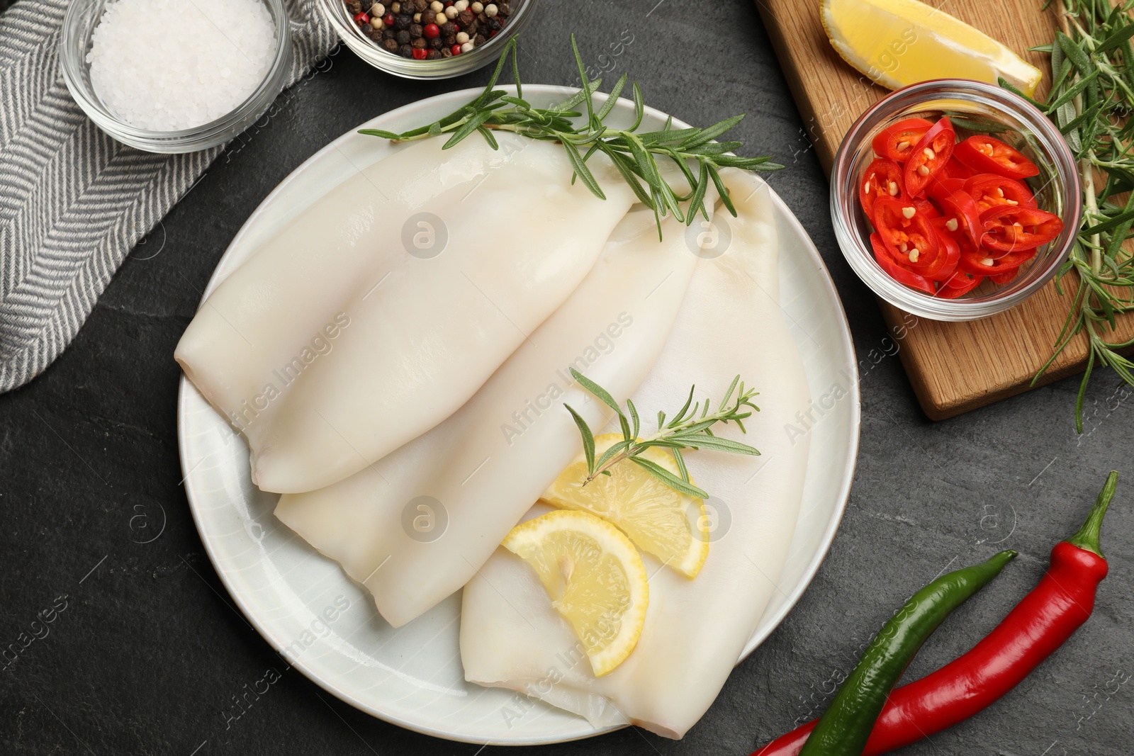 Uncooked squids with lemon slices, rosemary and spices on black table, flat lay Photo of Uncooked squids with lemon slices, rosemary and spices on black table, flat lay