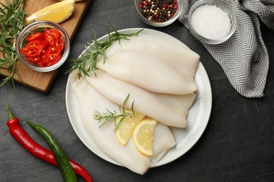 Photo of Uncooked squids with lemon slices, rosemary and spices on black table, flat lay