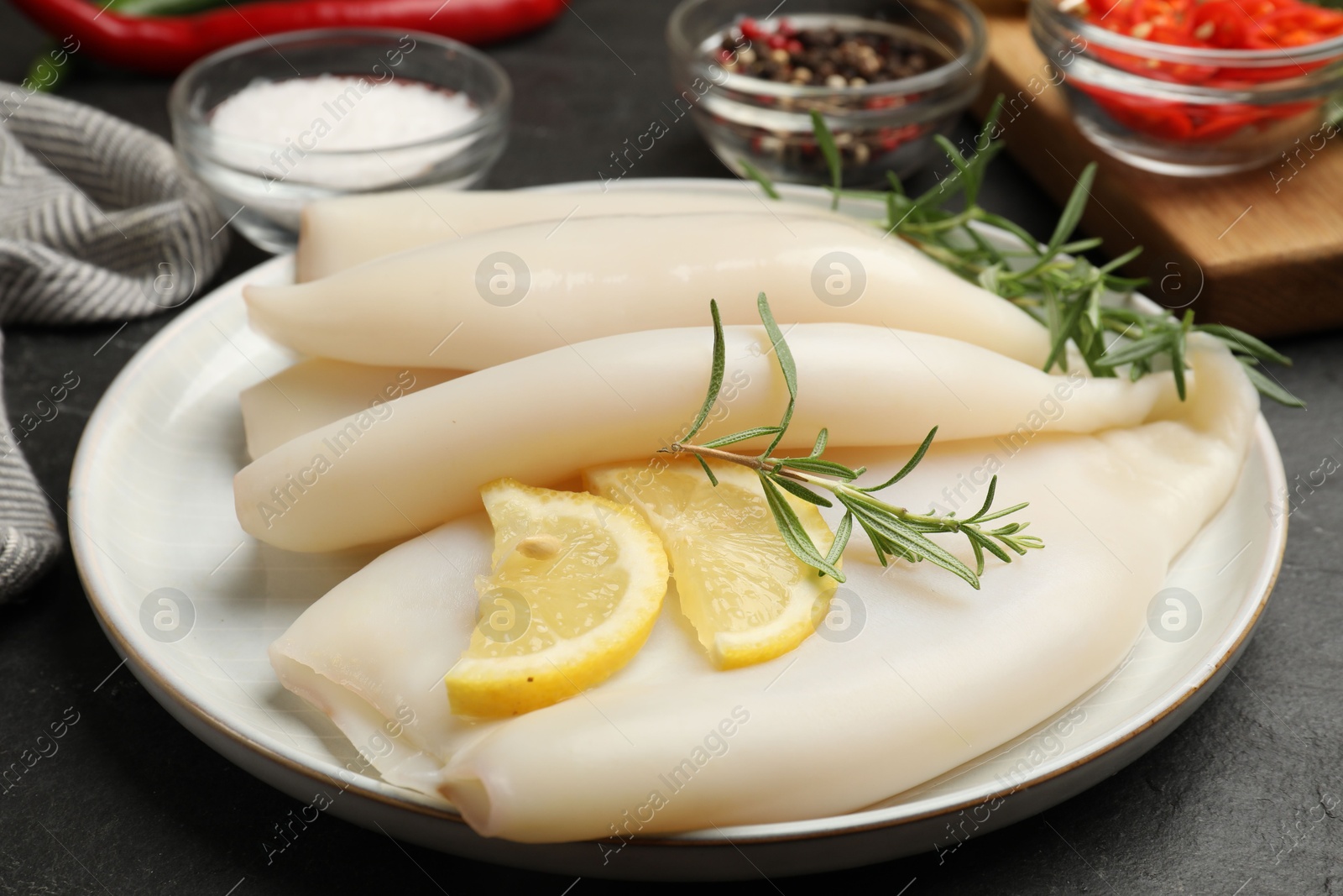 Uncooked squids with lemon slices, rosemary and spices on black table, closeup Photo of Uncooked squids with lemon slices, rosemary and spices on black table, closeup