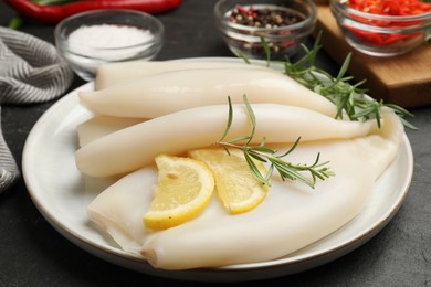 Photo of Uncooked squids with lemon slices, rosemary and spices on black table, closeup