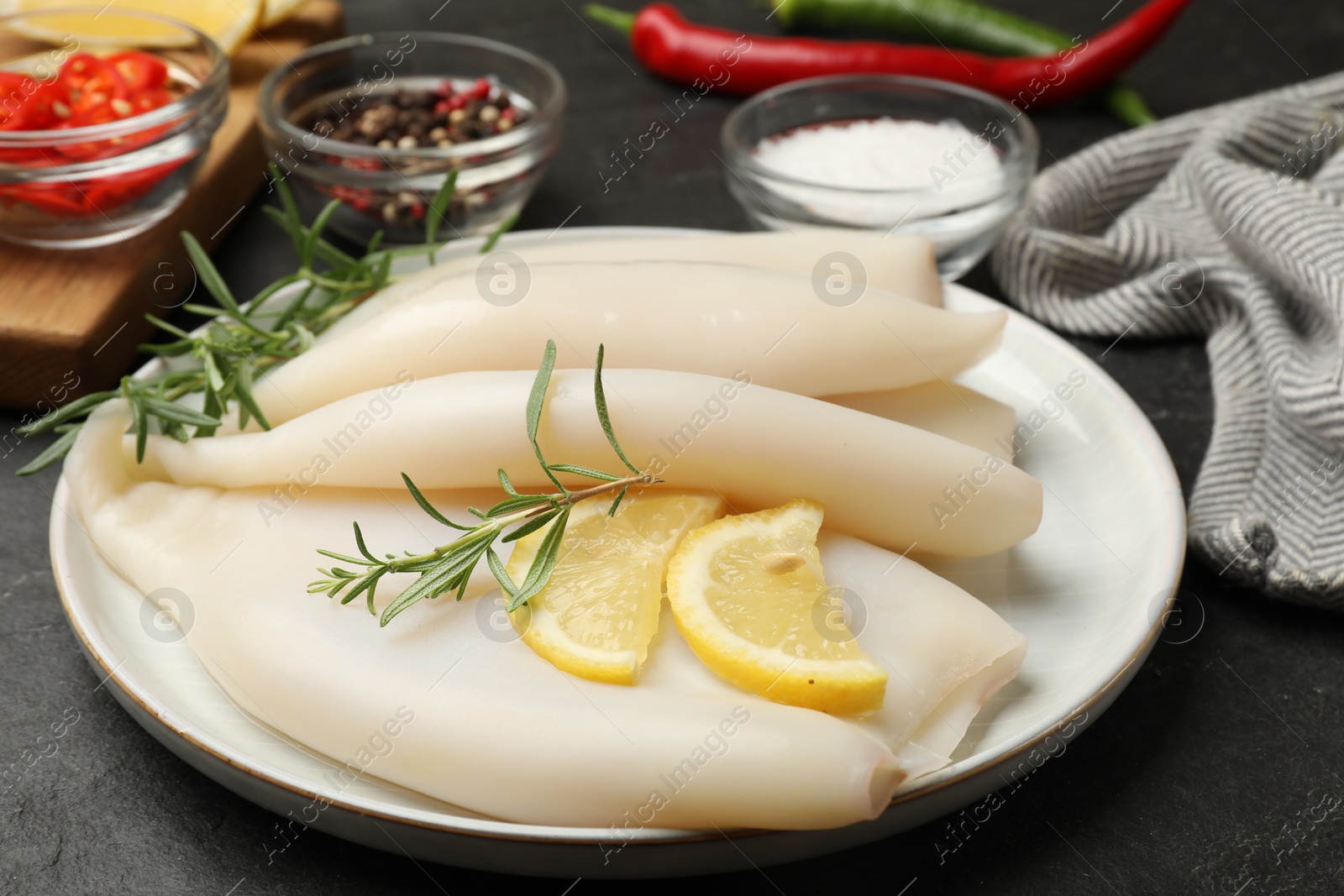 Uncooked squids with lemon slices, rosemary and spices on black table, closeup Photo of Uncooked squids with lemon slices, rosemary and spices on black table, closeup