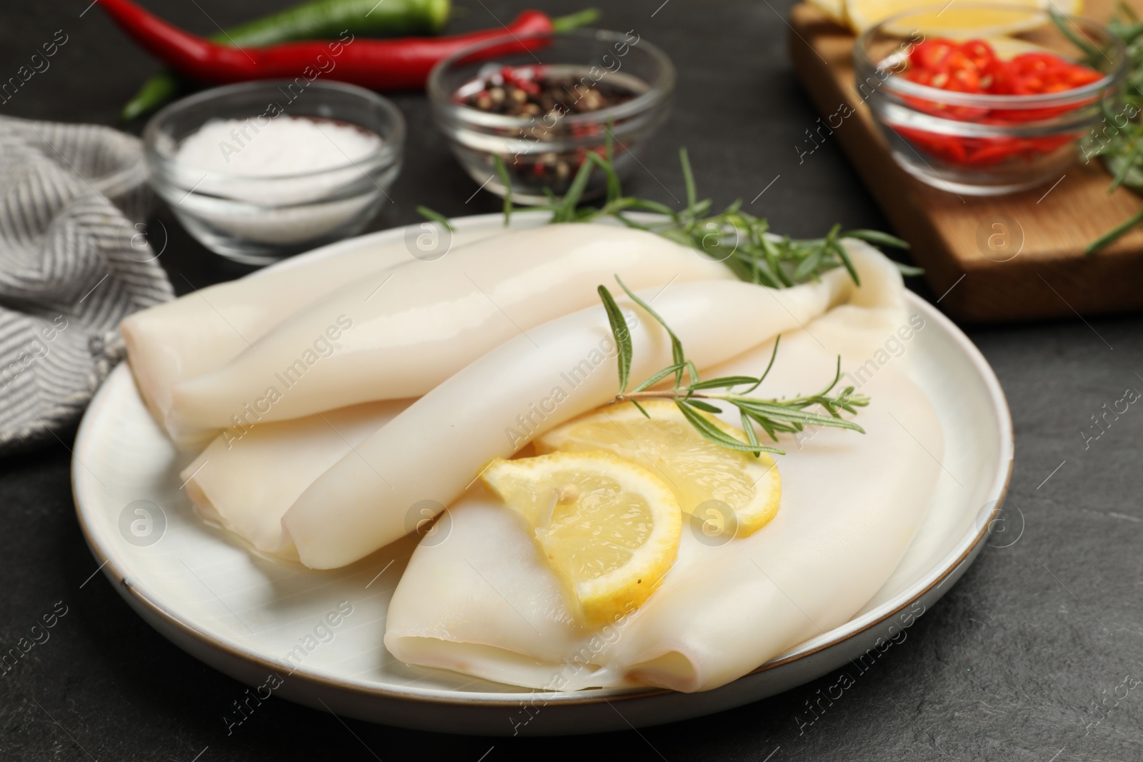 Uncooked squids with lemon slices, rosemary and spices on black table, closeup Photo of Uncooked squids with lemon slices, rosemary and spices on black table, closeup