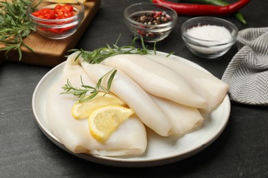 Photo of Uncooked squids with lemon slices, rosemary and spices on black table, closeup