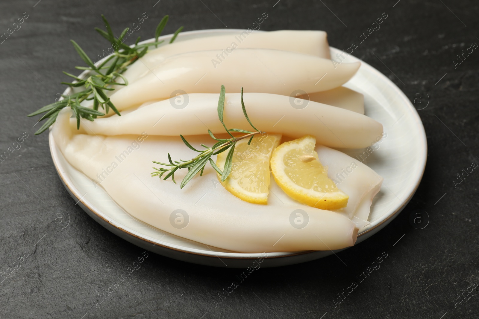 Uncooked squids with lemon slices and rosemary on black table, closeup Photo of Uncooked squids with lemon slices and rosemary on black table, closeup