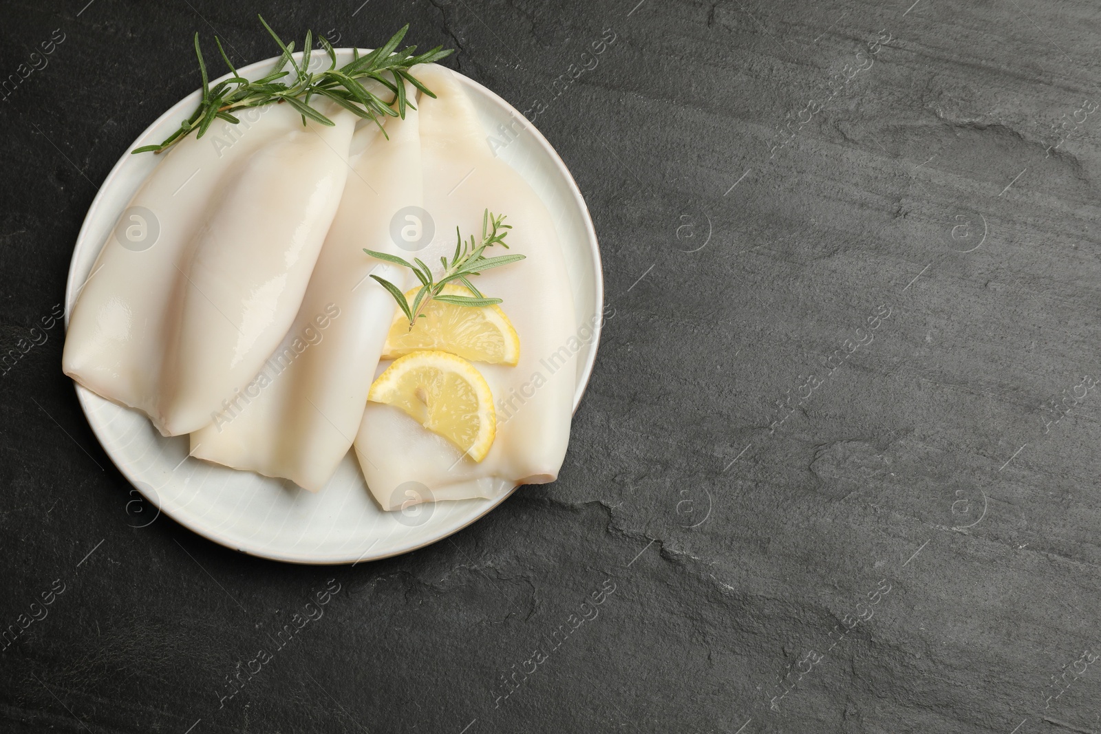 Uncooked squids with lemon slices and rosemary on black table, top view. Space for text Photo of Uncooked squids with lemon slices and rosemary on black table, top view. Space for text