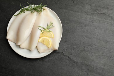 Photo of Uncooked squids with lemon slices and rosemary on black table, top view. Space for text